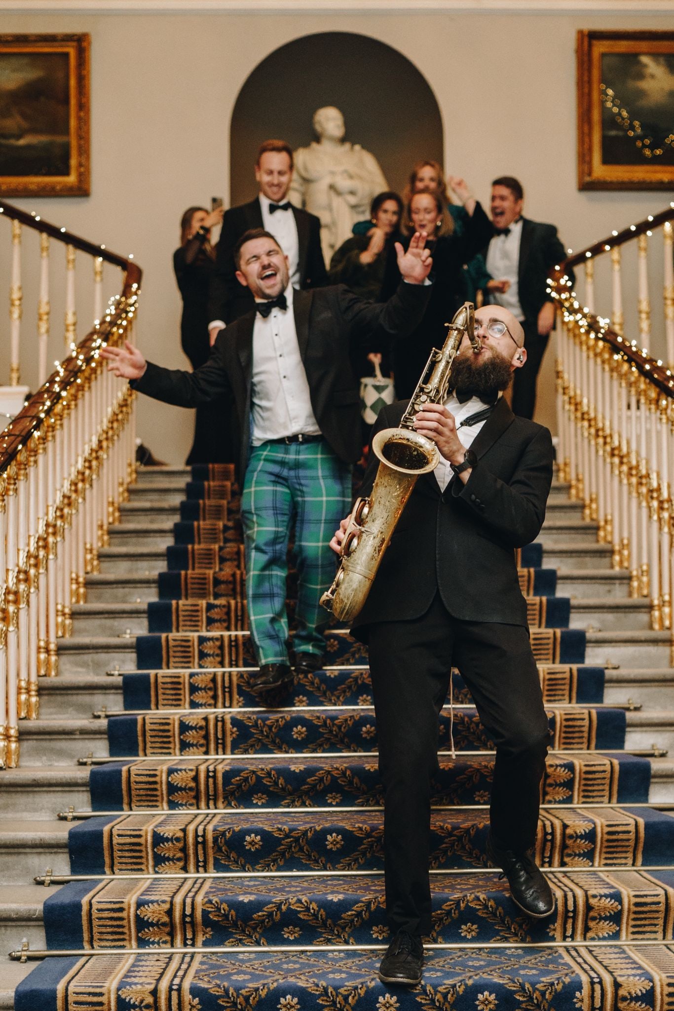 The saxophonist coming down a grand staircase, guests following