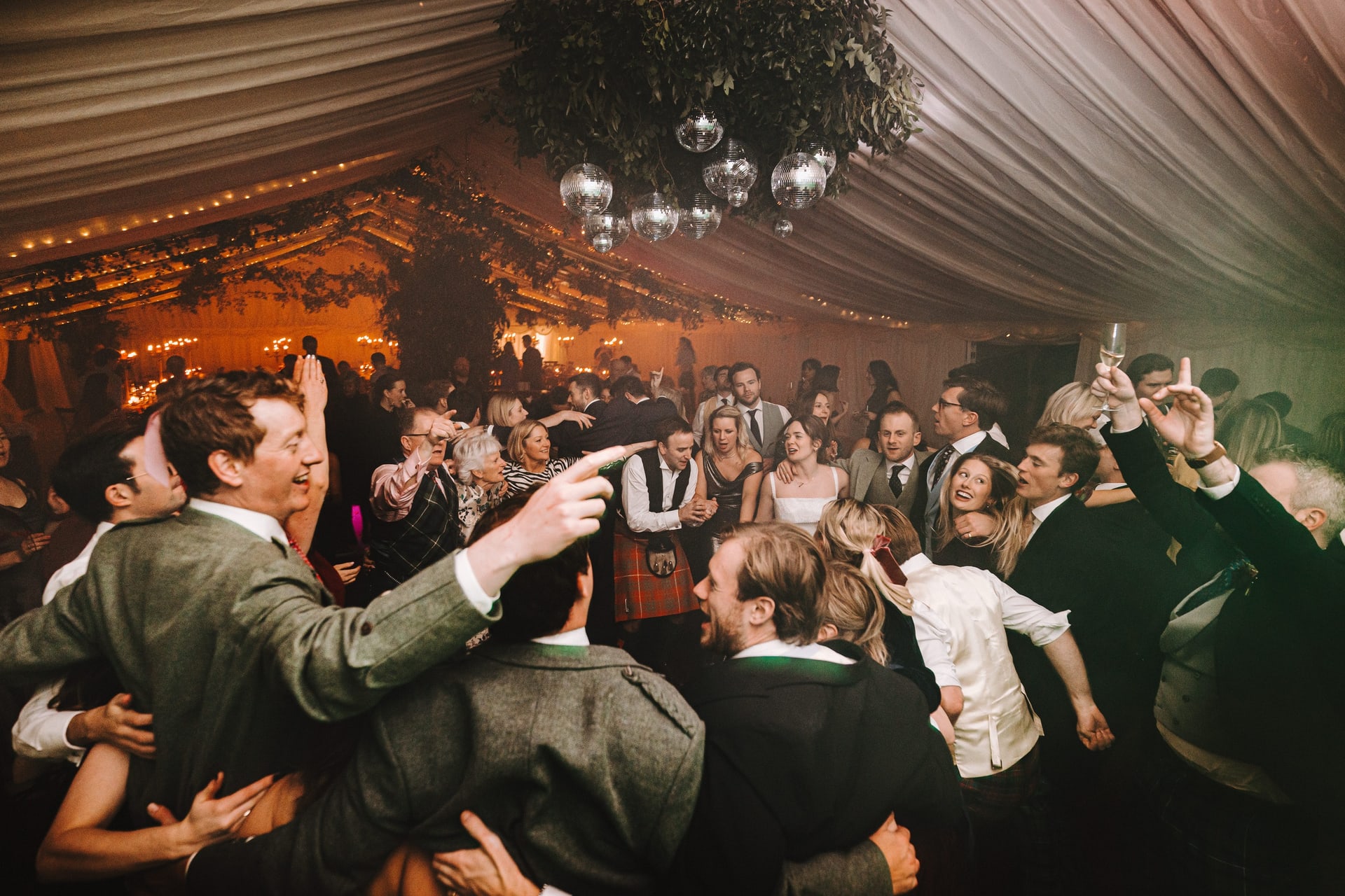 Guests dancing in a marquee lit warm under a canopy of lights